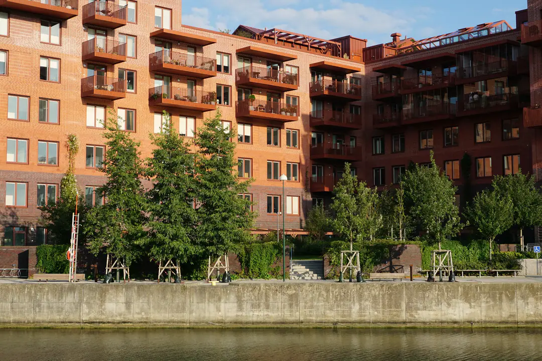 Wohnhäuser aus Backstein mit Balkonen hinter jungen Bäumen am Wasser